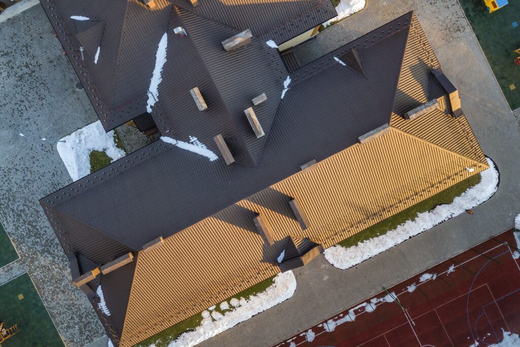 Top aerial view of building brown shingle tiled roof with complex configuration construction. Abstract background, geometrical pattern.